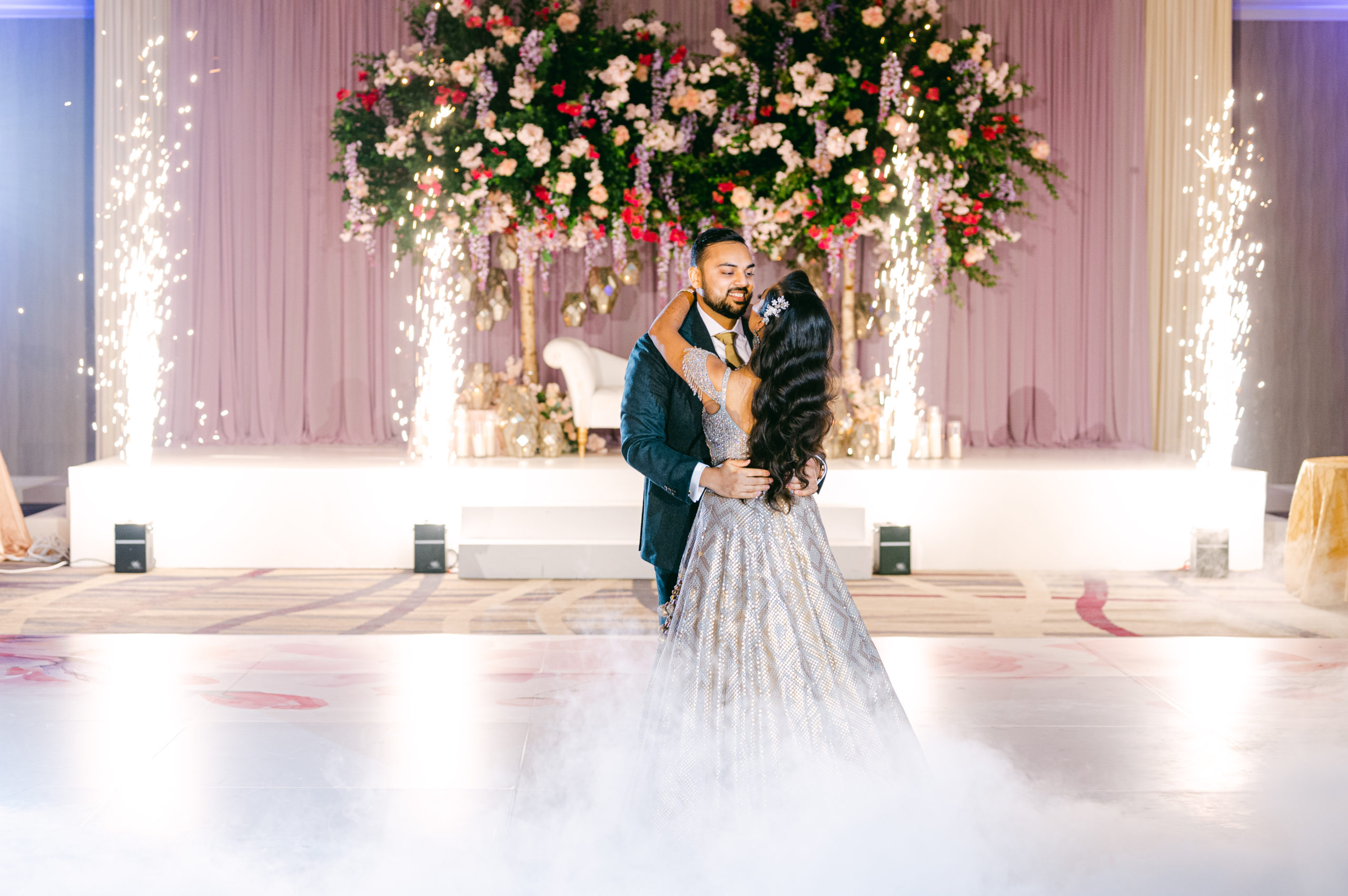 The Bride and Groom have their first dance. Sparklers go off in the background and fog is at their feet.