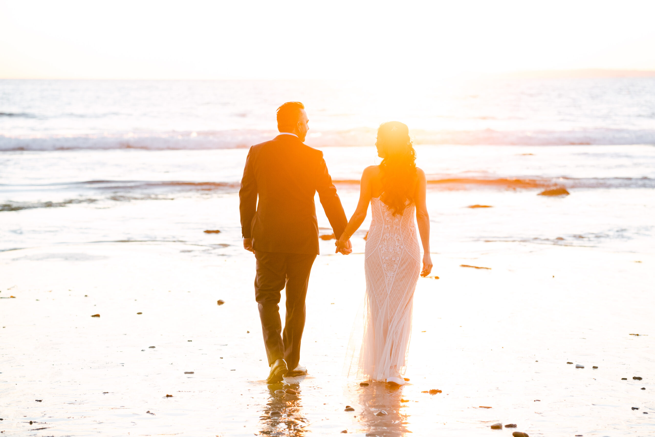 Stunning sunset wedding portrait of a bride and groom walking towards the water at sunset on Laguna Beach. Photo by Kate Noelle Photography